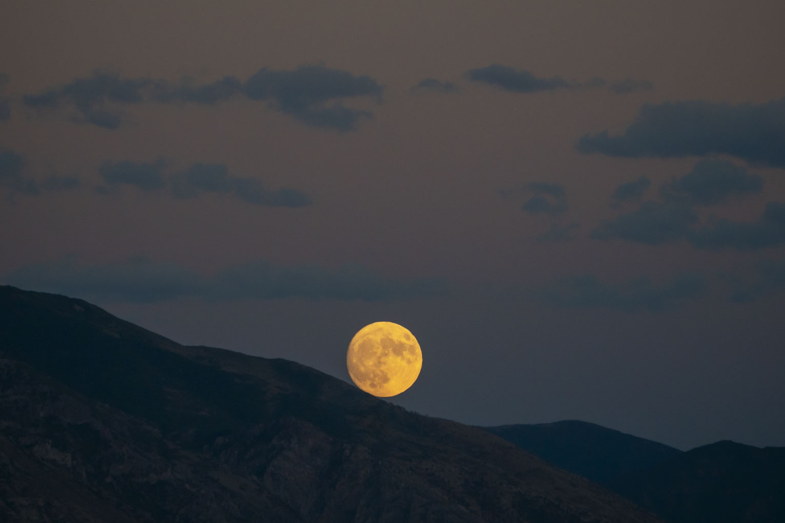 The rising full moon its edge still touching the mountainside